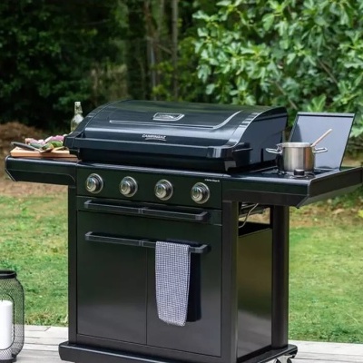 Churrasqueira de carvão preta com quatro botões e panela no lado direito num jardim