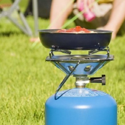 Fogão portátil de gás azul com panela preta num gramado verde