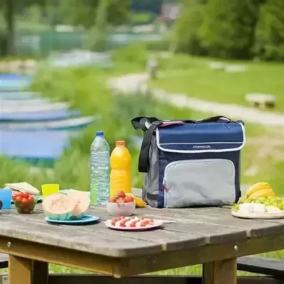 Mala térmica azul e cinza CAMPINGAZ sobre mesa de madeira com comida e bebidas ao ar livre