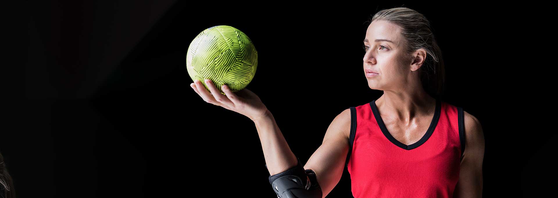 REMOZILL- Tira Resinas Mulher com colete desportivo vermelho e preto segurando bola verde com textura rugosa