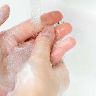 Mãos a lavar-se com água corrente em lavatório branco