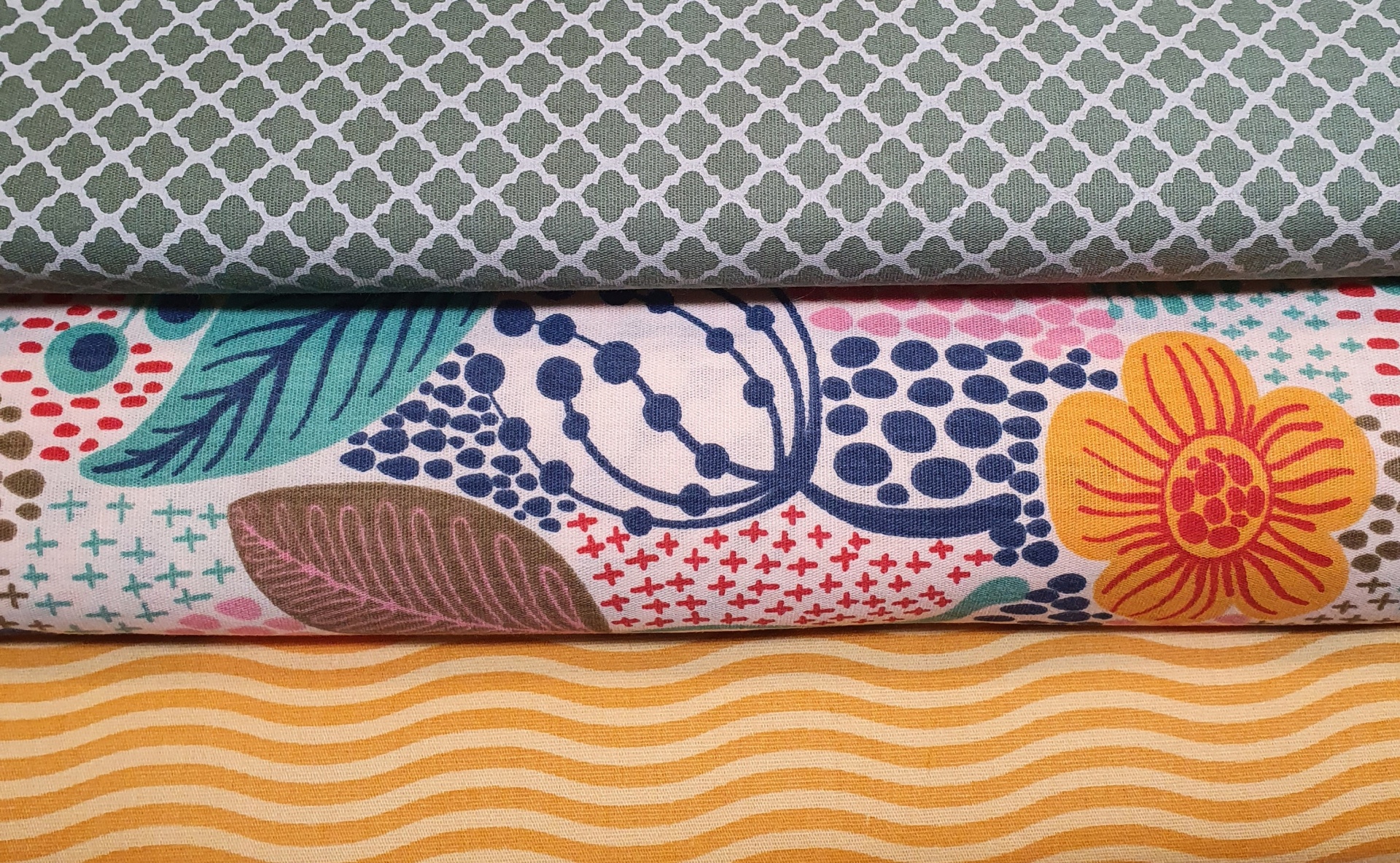 Contemporâneo 2 Três tecidos dobrados com padrões geométrico cinza, flores coloridas e ondulações amarelas.