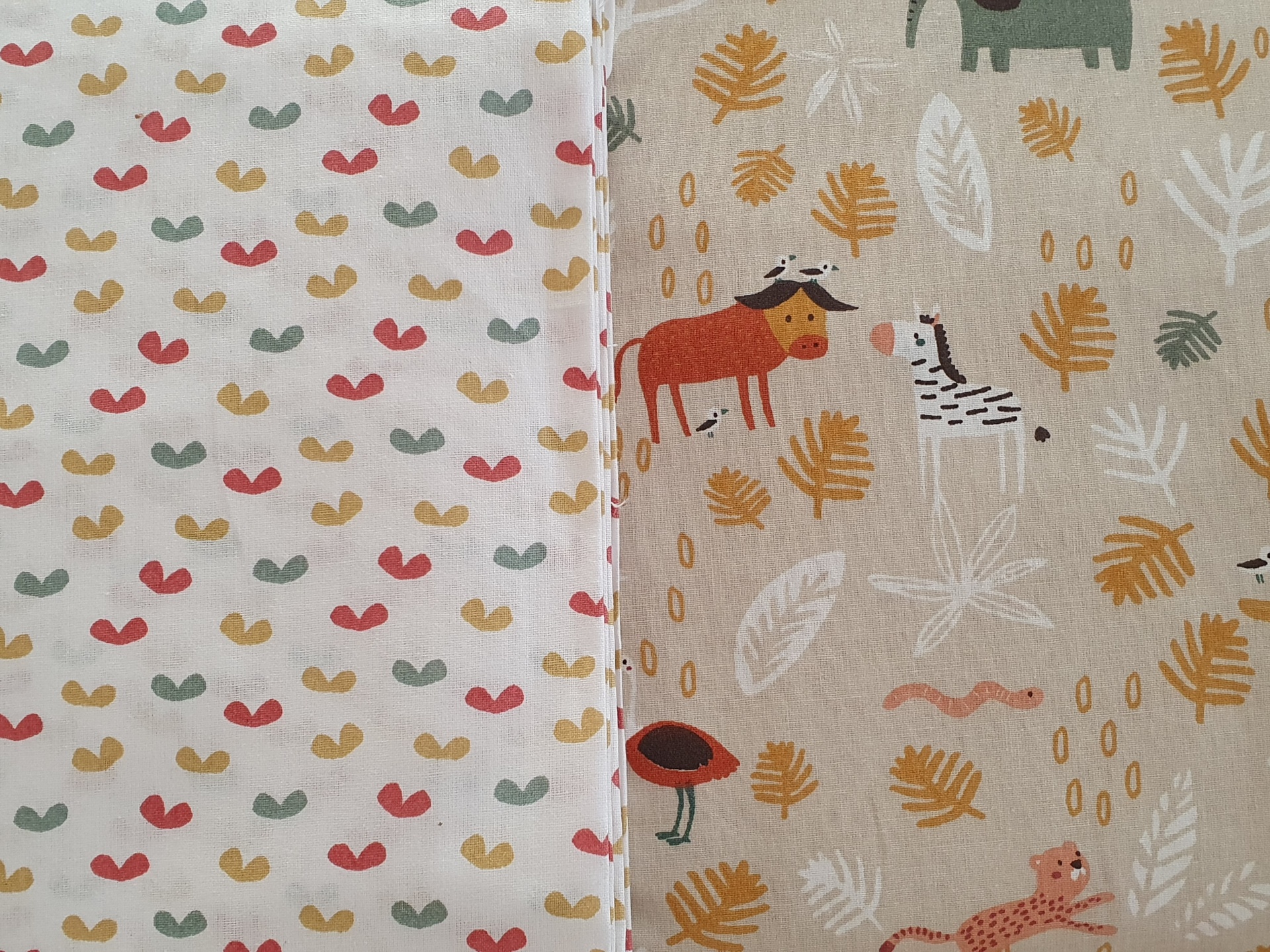 Little Jungle Dois tecidos lado a lado com padrões coloridos, um branco com formas pequenas e outro bege com animais e folhas.