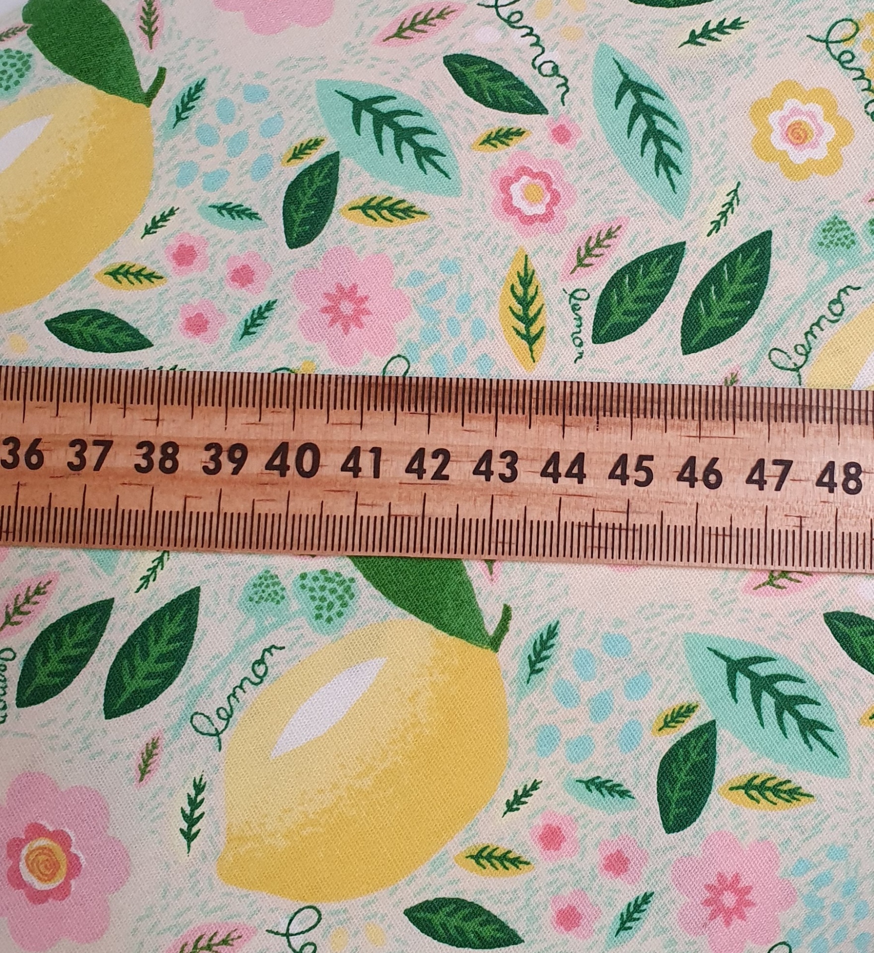 Folhas Limão Tecido estampado com limões, folhas e flores ao lado de régua de madeira.