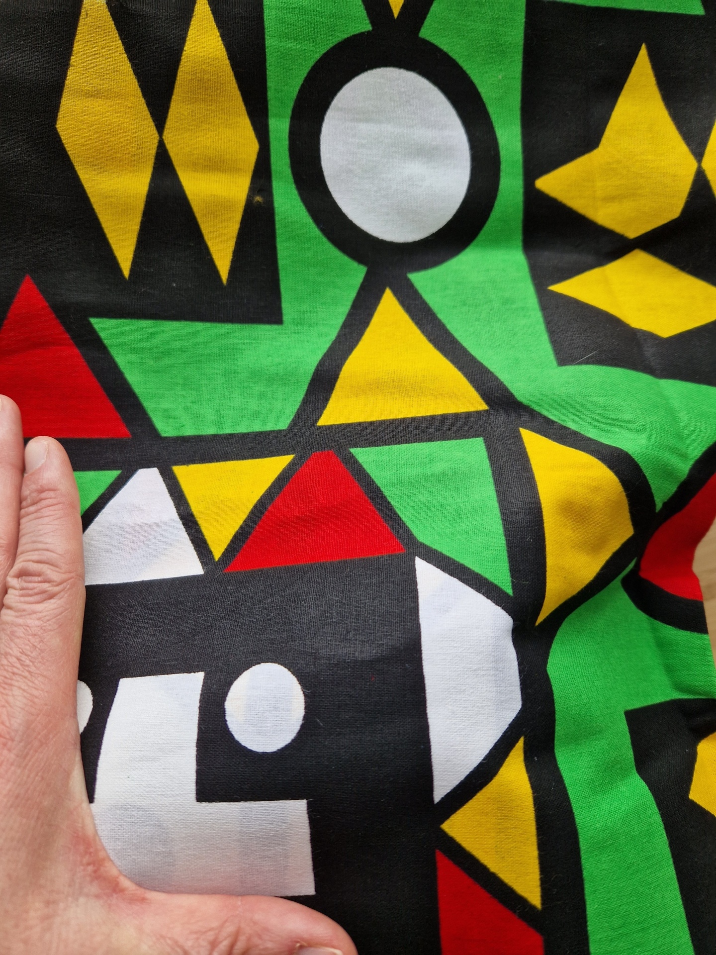 Capulana Samakaka Angola tecido colorido com padrão geométrico e mão sobre ele
