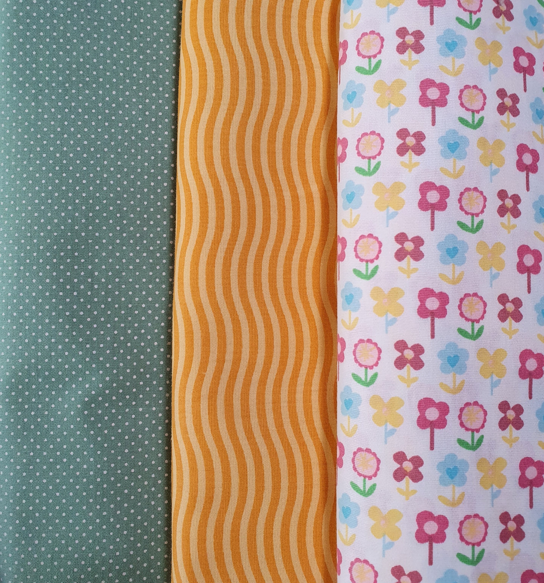 Rose Blossom Três tecidos com padrões distintos: verde com pontos, amarelo com ondas, branco com flores coloridas.