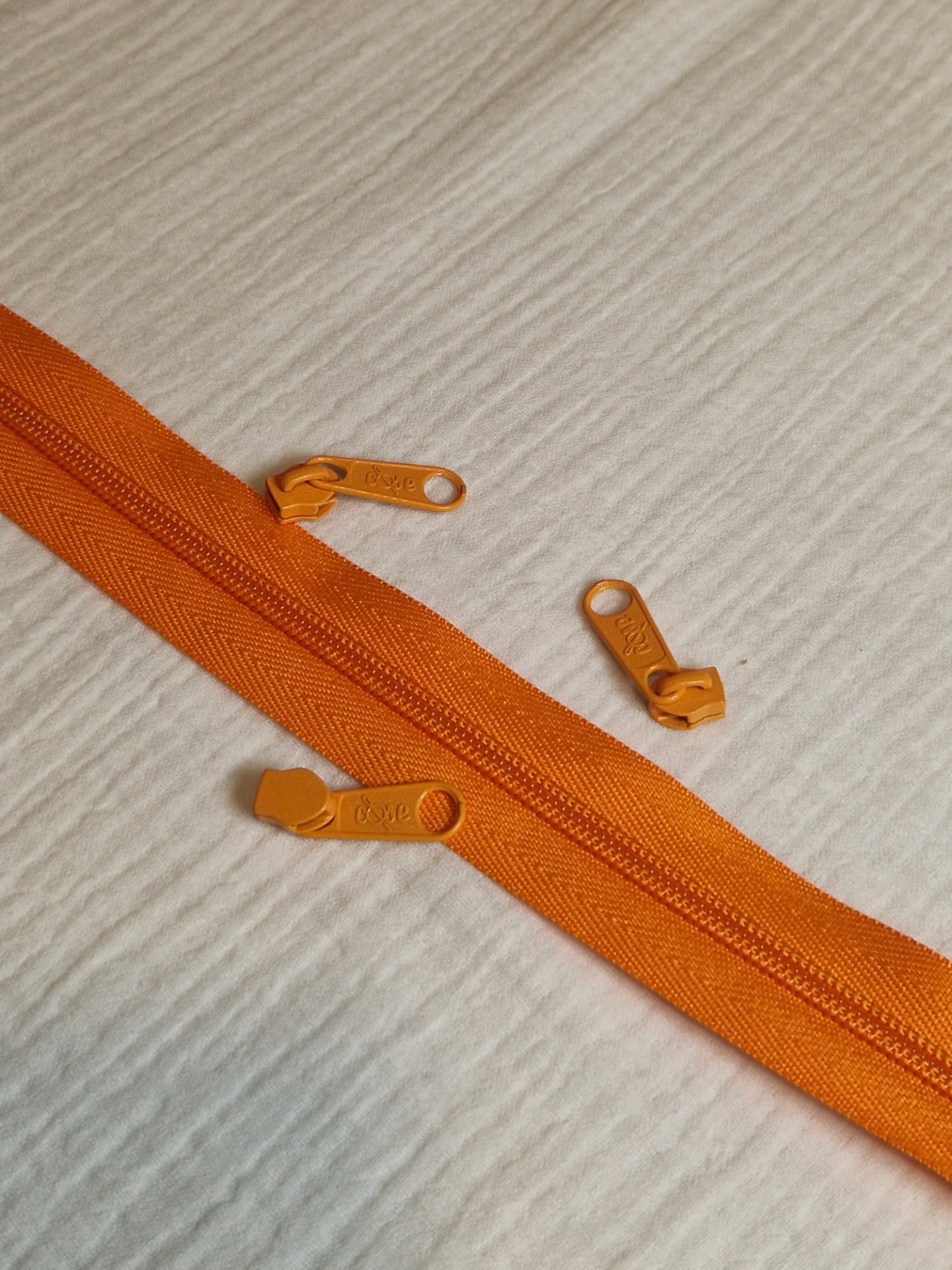 Fecho e cursor malha 5 Laranja Manga Fecho éclair laranja com três cursores amarelos sobre fundo de tecido claro