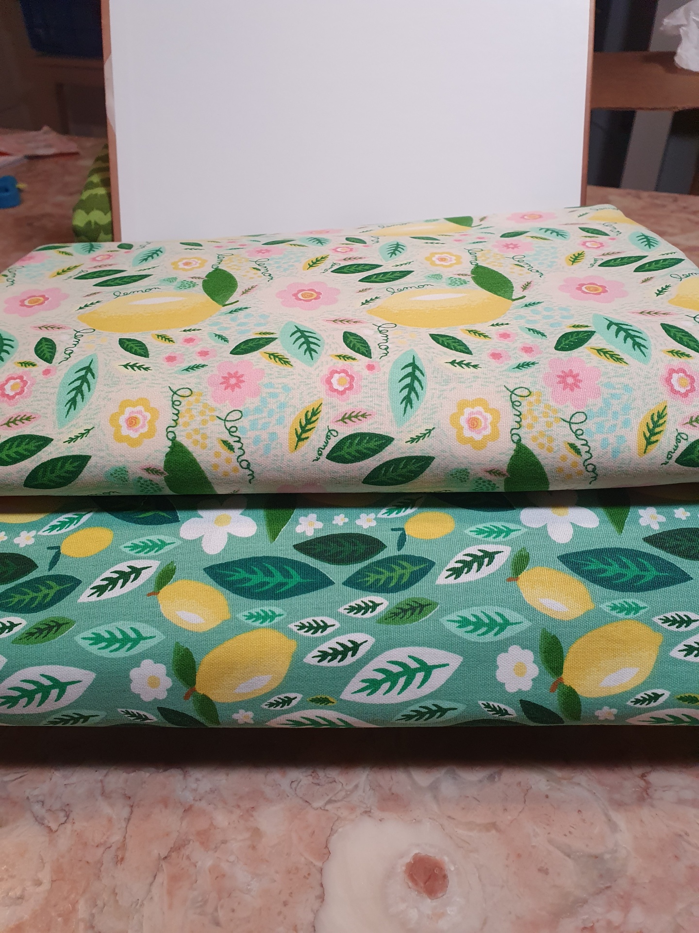 Folhas Limão Dois panos de tecido com padrão de limões, folhas e flores, um bege e outro verde.