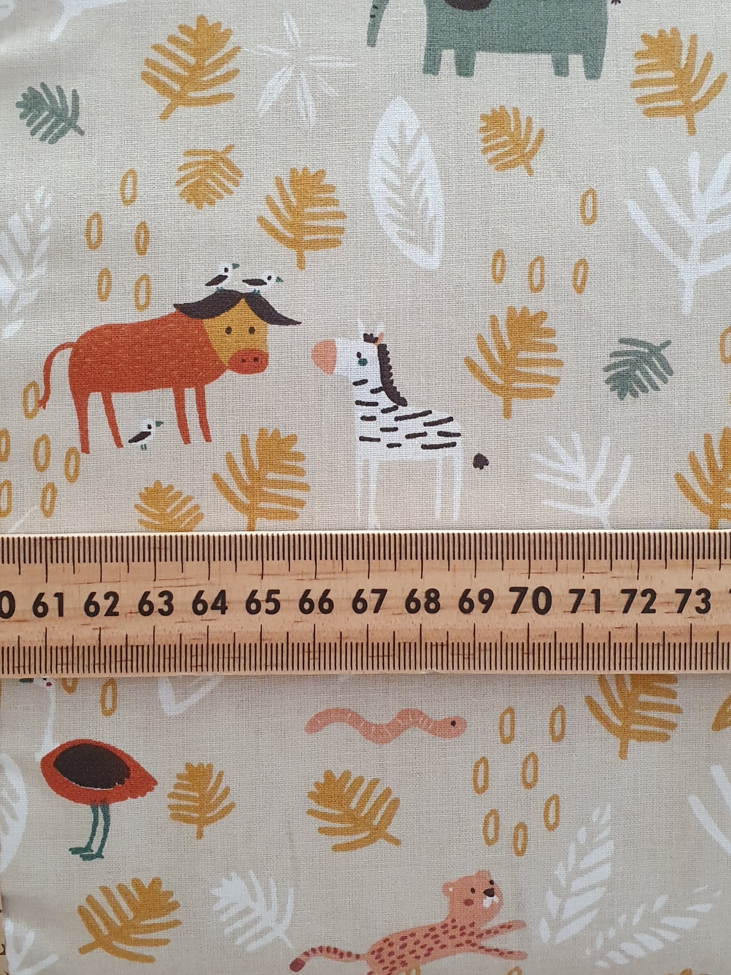 Little Jungle Tecido de algodão com padrão de animais e folhas, com régua de madeira sobreposta.