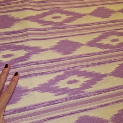 Tecido lilás e amarelo com padrão geométrico e mão com unhas castanho escuro