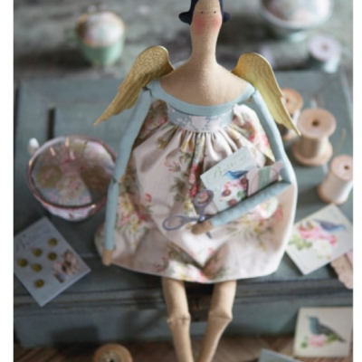 Boneca de tecido com vestido florido sentada sobre caixa cinza e acessórios de costura