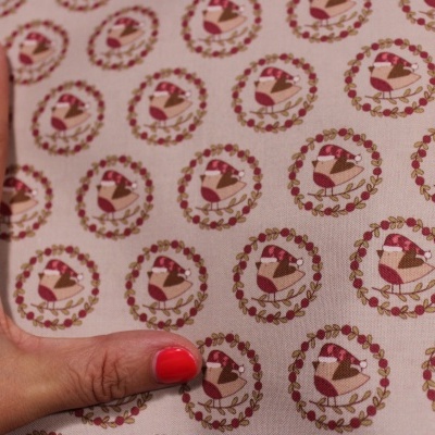 tecido bege com padrão de pássaros dentro de círculos florais e mão com unhas vermelhas