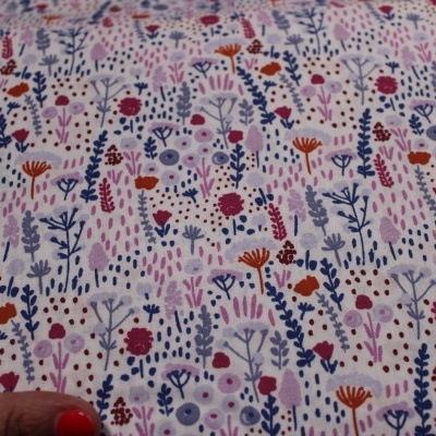 Tecido floral colorido sobre fundo branco, segurado por mão com unhas vermelhas