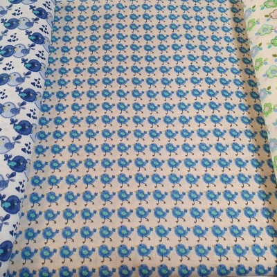 Três rolos de tecido com padrões de pássaros e flores em cores azuis, verdes e castanhas