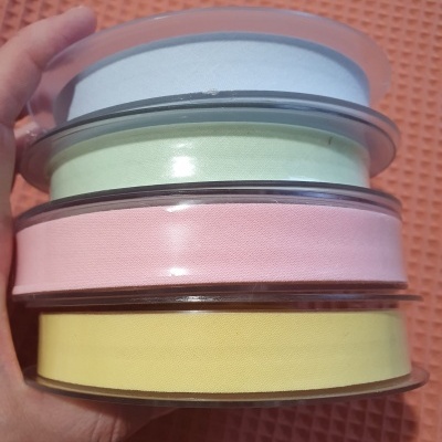 Quatro rolos de fita de tecido em cores pastel em carretéis plásticos, sobre fundo laranja texturizado