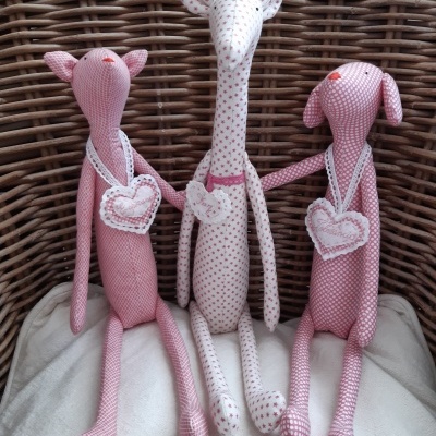 Bonecos de tecido rosa com corações, sentados em fundo de vime.