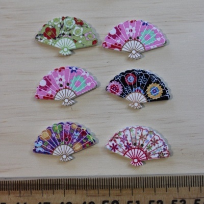 Seis miniaturas coloridas de leques decorativos sobre madeira clara com régua para escala