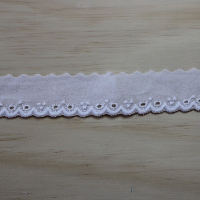 Fita branca bordada com padrão floral sobre madeira clara