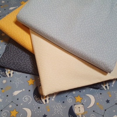 Tecidos dobrados com padrões finos em várias cores sobre tecido azul com estrelas e luas