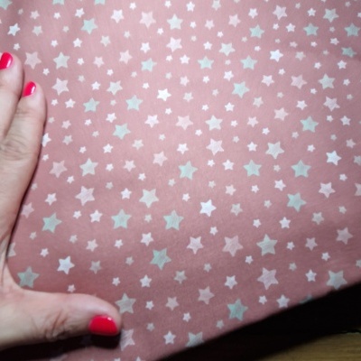 tecido cor de rosa com padrão de estrelas brancas e azuis claros e mão com unhas vermelhas