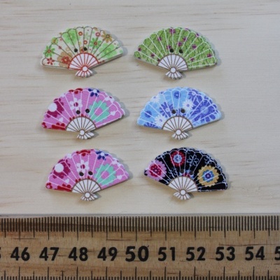 Seis pequenos leques decorativos coloridos sobre fundo de madeira com régua embaixo.