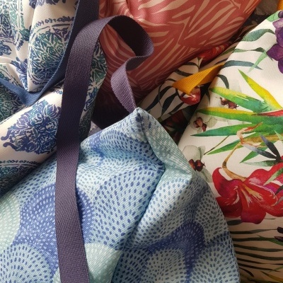 Quatro mochilas de tecido com padrões coloridos e alças, incluindo motivos florais e folhas.
