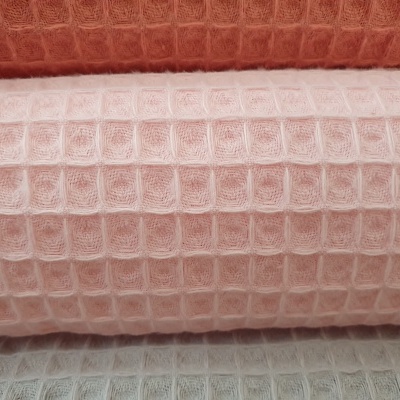 Três rolos de tecido em padrão xadrez com textura em waffle, nas cores laranja, rosa claro e cinza claro.