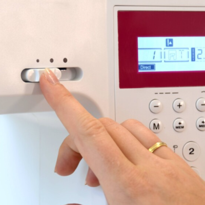 Máquina de costura branca com painel digital vermelho e mão ajustando botão.