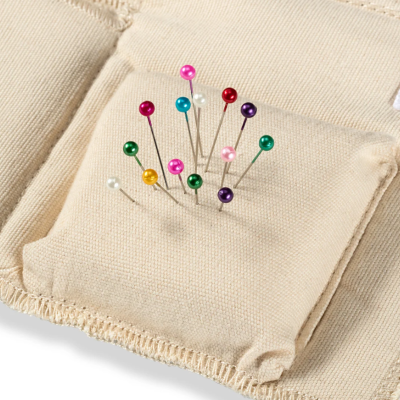 Alfinetes coloridos presos numa pequena almofada de tecido bege