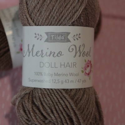 Novelo de lã Merino castanha claro com etiqueta Tilda Merino Wool Doll Hair sobre fundo rosa