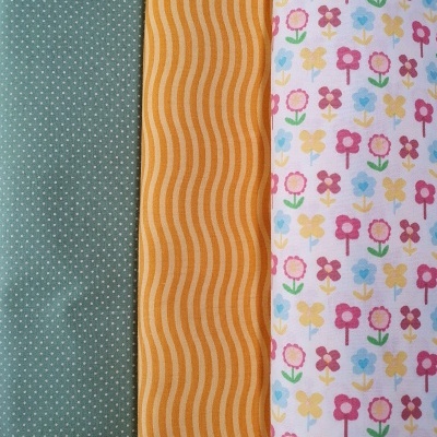 Três tecidos com padrões distintos: verde com pontos, amarelo com ondas, branco com flores coloridas.