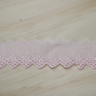 Faixa de tecido rosa claro com bordado floral em ziguezague sobre madeira clara