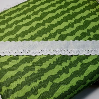 Fita decorativa branca sobre tecido verde com padrão ondulado.