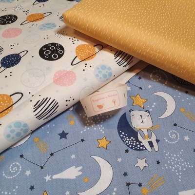 Três tecidos coloridos com padrões de planetas, raposa na lua, estrelas e linhas brancas.