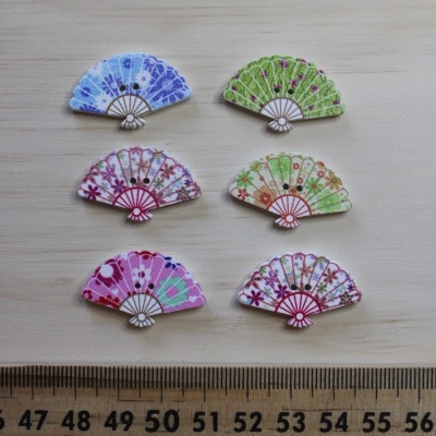 Seis botões em forma de leque colorido com padrões florais, em madeira, sobre fundo de madeira clara e régua de madeira para escala.