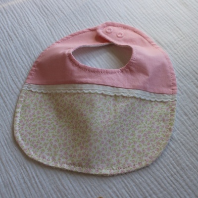 Babete de bebé rosa e branco com padrão floral e renda