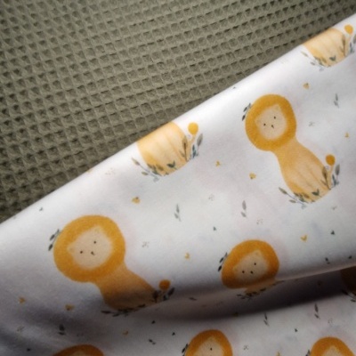 Dois tecidos, um verde cinzento com padrão de colmeia e outro branco com padrão de leões amarelos.