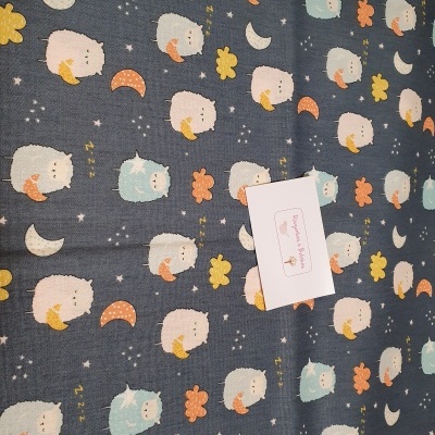 tecido azul escuro com estampado de ovelhas, luas, nuvens e estrelas e um cartão branco no centro