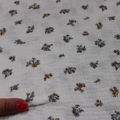 pano branco com padrão de flores pequenas azuis e castanhas, mão com unhas vermelhas segurar pano