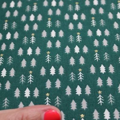 Tecido verde com padrão de pequenas árvores brancas e douradas e mão com unhas vermelhas
