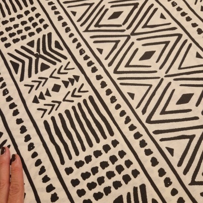 tecido branco com padrões geométricos pretos e mão feminina a tocar