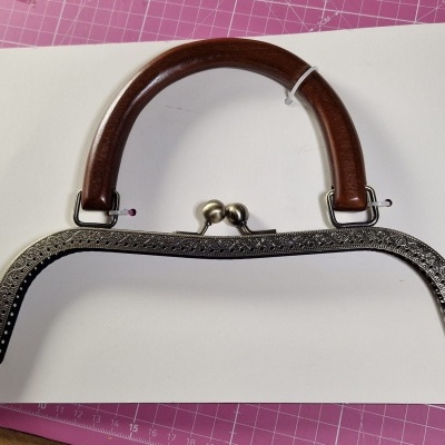 Armação metálica prateada com alça castanha em fundo branco e rosa