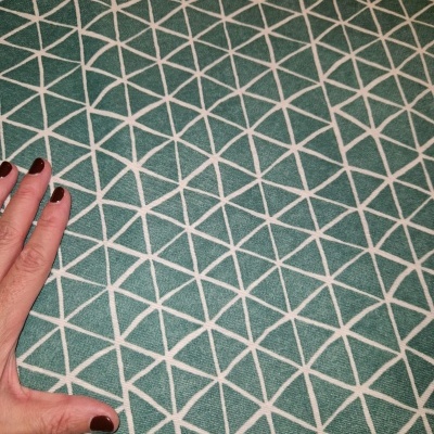 tecido verde-azulado com padrão geométrico branco e mão feminina ao lado