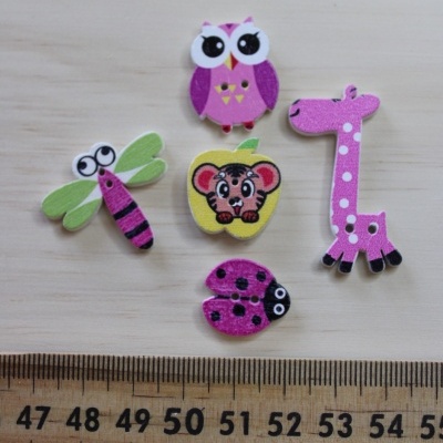 Botões decorativos coloridos em formas de animais e maçã sobre superfície de madeira clara com régua.