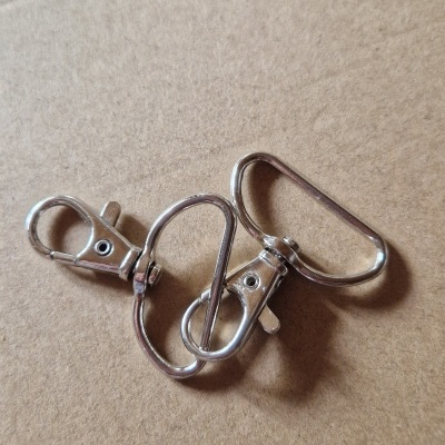 Três mosquetões metálicos prateados e uma argola retangular sobre superfície castanha