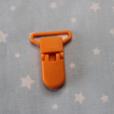 Clipe de plástico laranja para chupeta sobre tecido azul com estrelas.