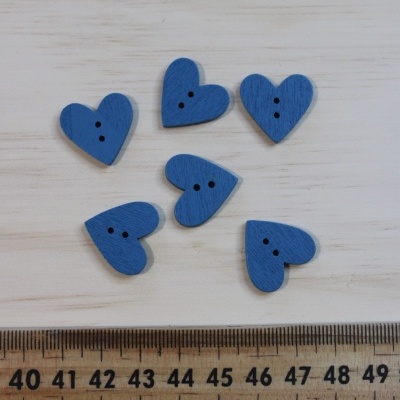 Seis botões azuis em forma de coração com dois furos, junto a uma régua de madeira.