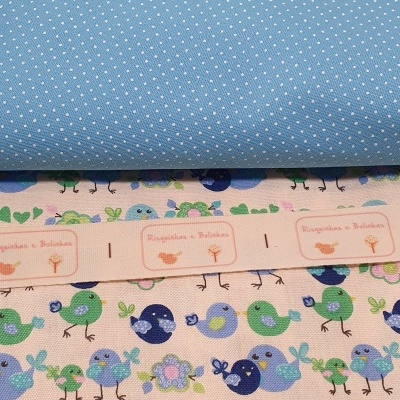 Tecidos azul com pontos brancos, tecido com pássaros em azul e verde e fita com etiquetas risquinhas e bolinhas