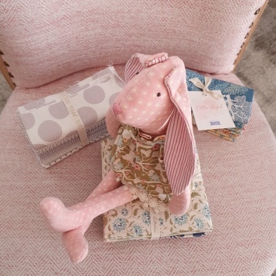 Boneca de coelho rosa em tecido sentada sobre tecidos estampados em cadeira rosa