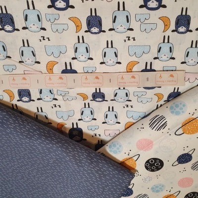 Três tecidos com padrões de coelhos, linhas e círculos coloridos sobre uma superfície plana, com régua rosa em cima.